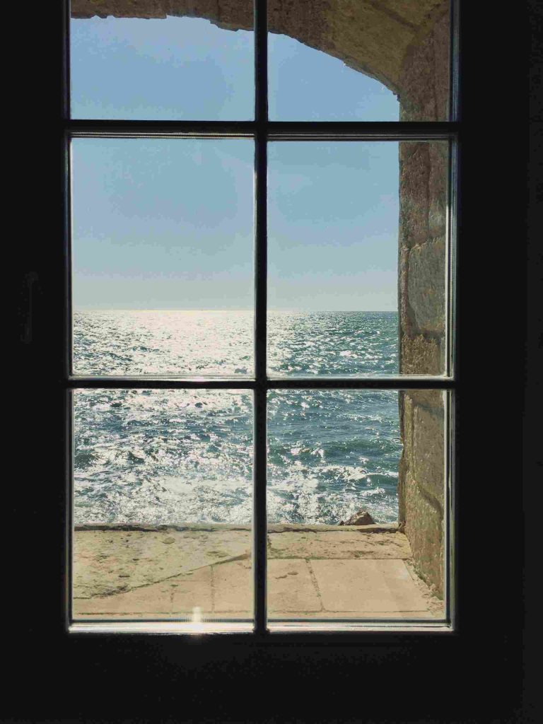 Window looking out to ocean sun shining on water
